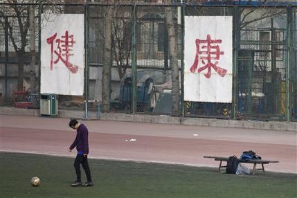 In this Saturday, Jan. 19, 2013 photo. a college student kicks a soccer ball in front of Chinese characters on the fence reading "good health" in Beijing. Despite its formidable performance in recent Olympic Games, China has found itself in a crisis of declining fitness among its youngsters. (AP Photo/Alexander F. Yuan)