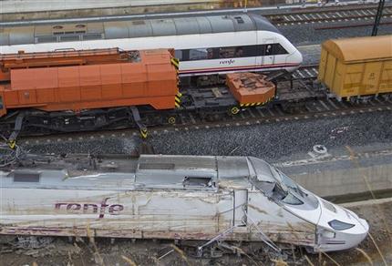 A passenger train passes the wreckage of a train in Santiago de Compostela, Spain, Saturday July 27, 2013. Spain's interior minister Jorge Fernandez Diaz says the driver whose speeding train crashed, killing 78 people, is now being held on suspicion of negligent homicide. The Spanish train  derailed at high speed Wednesday killing 78 and injuring dozens more. (AP Photo/Lalo R. Villar)