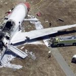 In this Saturday, July 6, 2013 aerial photo, firefighters, lower center, stand by a tarpaulin sheet covering the body of a Chinese teen struck by a fire truck during the emergency response to the crash of Asiana Flight 214 at the San Francisco International Airport in San Francisco. The girl was hit by a fire truck while covered with firefighting foam, authorities said Friday, July 12, revealing a startling detail that suggested she could have survived the crash only to die in its chaotic aftermath. (AP Photo/Marcio Jose Sanchez)