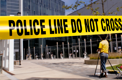 Crime scene tape with a camerman in the near background and a SWAT team in the far background.