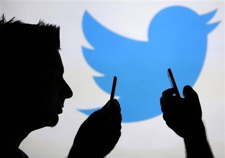 Men are silhouetted against a video screen with an Twitter logo as he poses with an Samsung S4 smartphone in this photo illustration taken in the central Bosnian town of Zenica