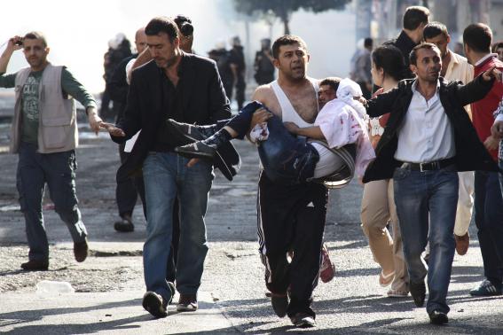 Injured Kurdish protester is carried by his friend as they clash with riot police in Diyarbakir