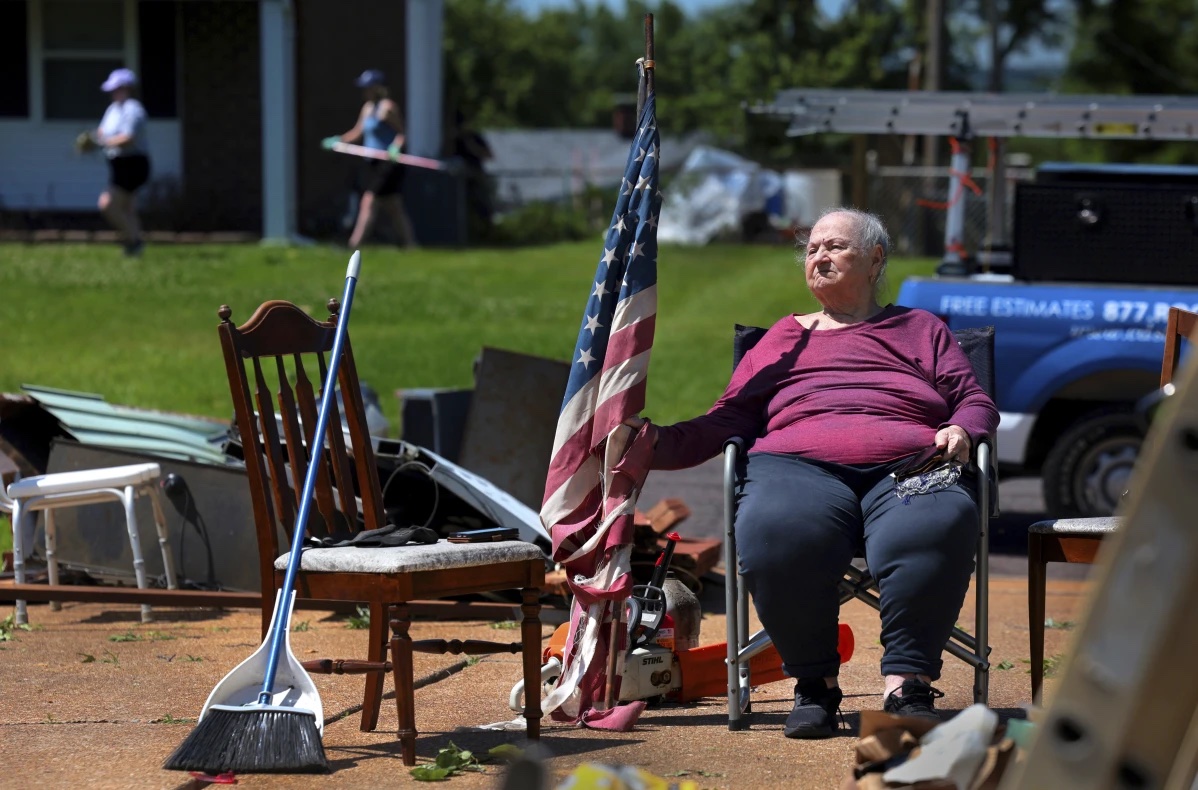 Jackie Moloney, 88, hangs on to her shredded American flag on Monday, May 27, 2024 as her family cleans up on Morningdale Place in Mehlville, Mo. 