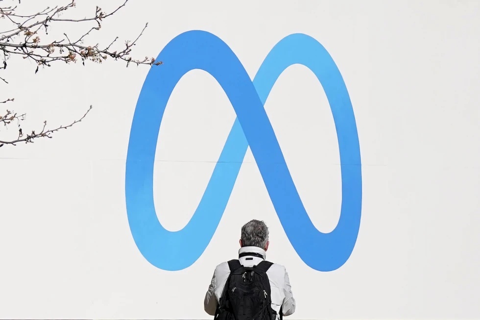 A person stands in front of a Meta sign outside of the company’s headquarters in Menlo Park