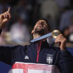 Serbia’s Novak Djokovic shows his gold medal after defeating Spain’s Carlos Alcaraz in the men’s singles tennis final at the Roland Garros stadium during the 2024 Summer Olympics, Sunday, Aug. 4, 2024