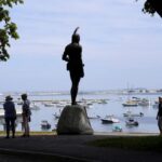 Visitors stand near a 1921 statue of the Wampanoag leader Massasoit, center, Wednesday, June 9, 2021, on Cole’s Hill, in Plymouth, Mass.