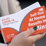 A woman holds two boxes of at-home Covid-19 test kits in Washington, Dec. 22, 2021.