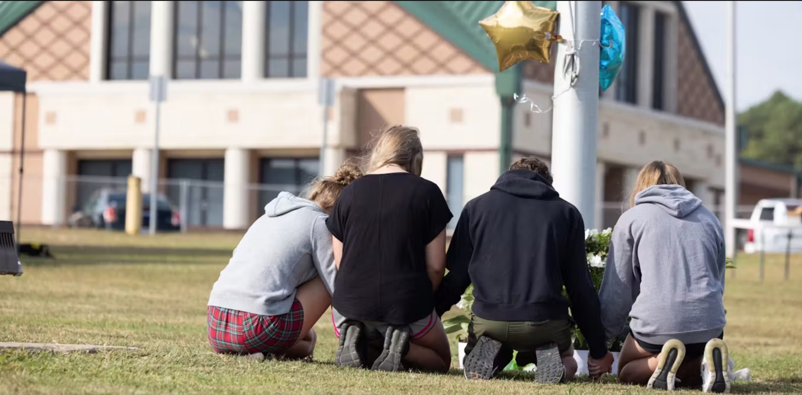 Students kneel in front of a makeshift memorial on Sept. 5, 2024, in front of Apalachee High School in Winder, Ga., where two students and two teachers were shot and killed the day before. 