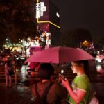 People look at their phones while waiting to cross an intersection in the rain at the Taikoo Li Sanlitun shopping center in Beijing, July, 30, 2024.