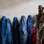 A Taliban fighter stands guard as women wait to receive food rations distributed by a humanitarian aid group in Kabul, Afghanistan, on May 23, 2023.