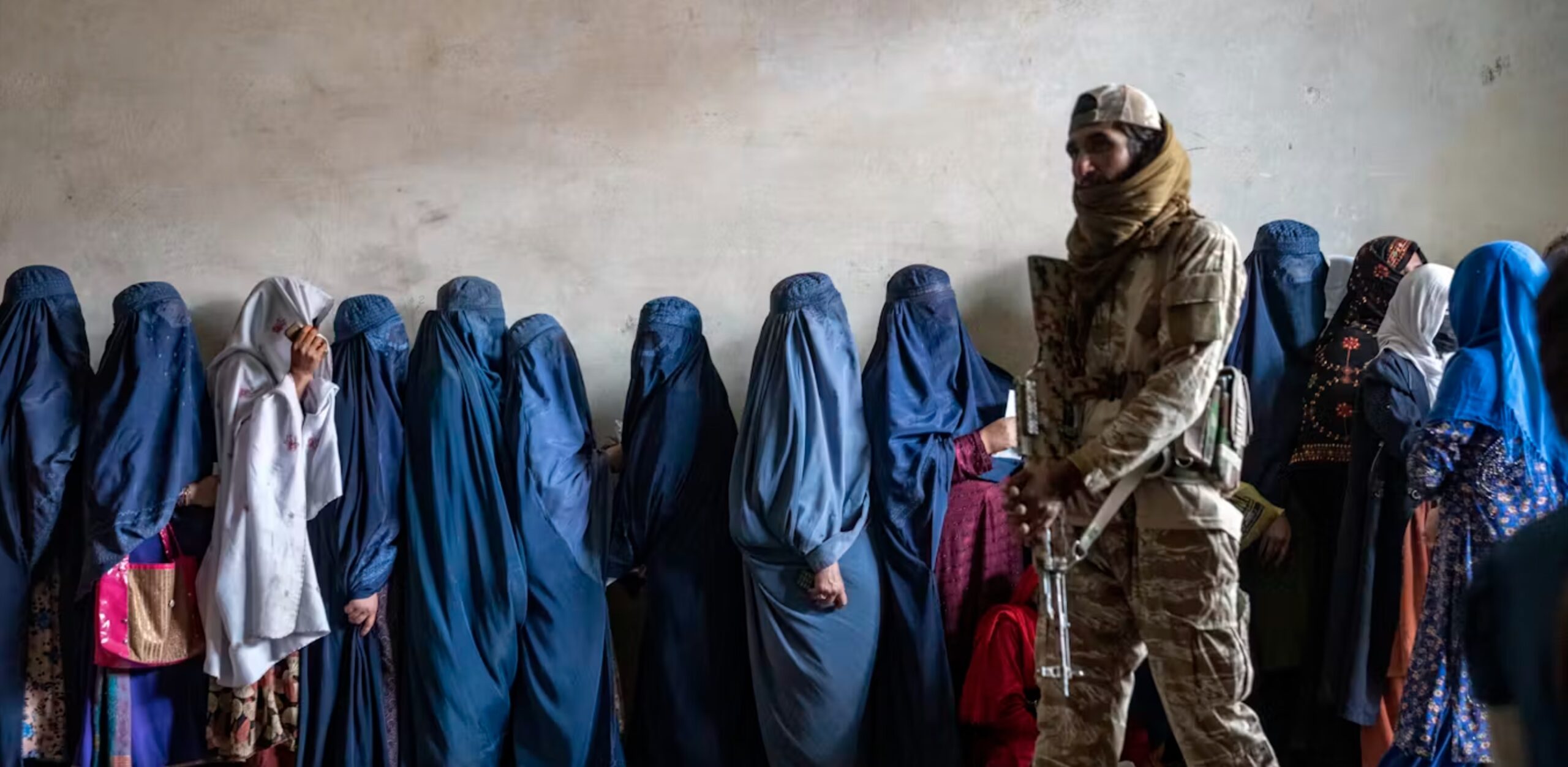 A Taliban fighter stands guard as women wait to receive food rations distributed by a humanitarian aid group in Kabul, Afghanistan, on May 23, 2023. 