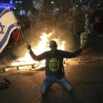 A protester holds an Israeli flag as Israelis light a bonfire during a protest after Prime Minister Benjamin Netanyahu has dismissed his defense minister Yoav Gallant in a surprise announcement in Tel Aviv, Israel, Tuesday, Nov. 5, 2024.