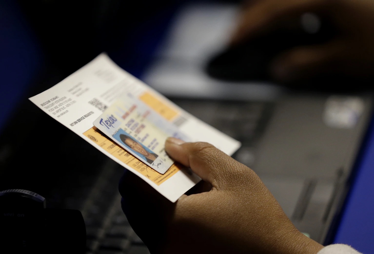 An election official checks a voter’s photo identification at an early voting polling site in Austin, Texas, Feb. 26, 2014.