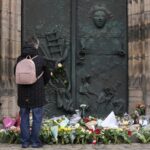 A person stands by flowers and candles placed outside St. John’s Church near a Christmas Market, where a car drove into a crowd on Friday evening, in Magdeburg, Germany, Saturday, Dec. 21, 2024.