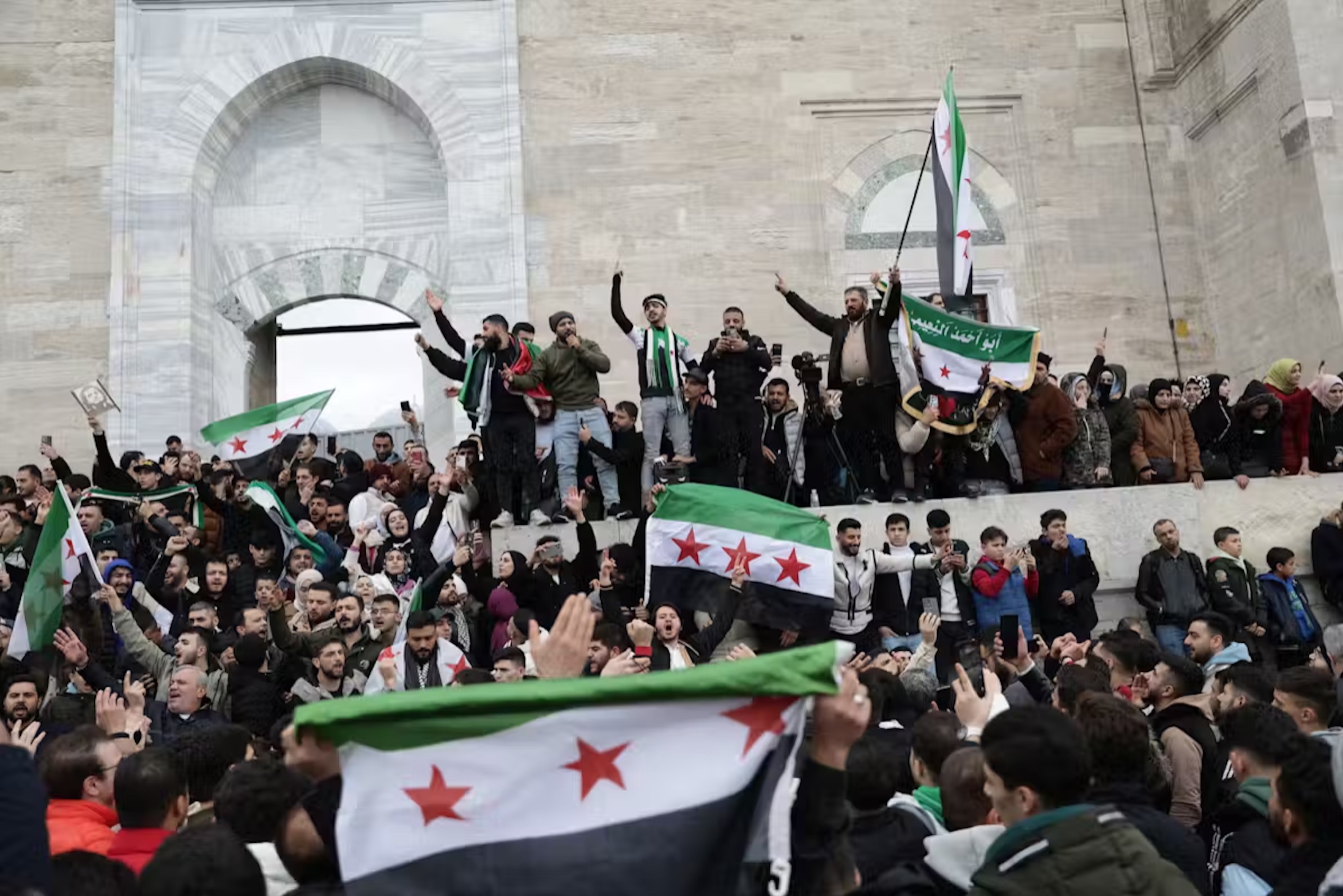 Supporters of the Syrian opposition residing in Turkey wave the Syrian flag of the opposition and celebrate the rebel takeover of Damascus a mosque in Istanbul. 