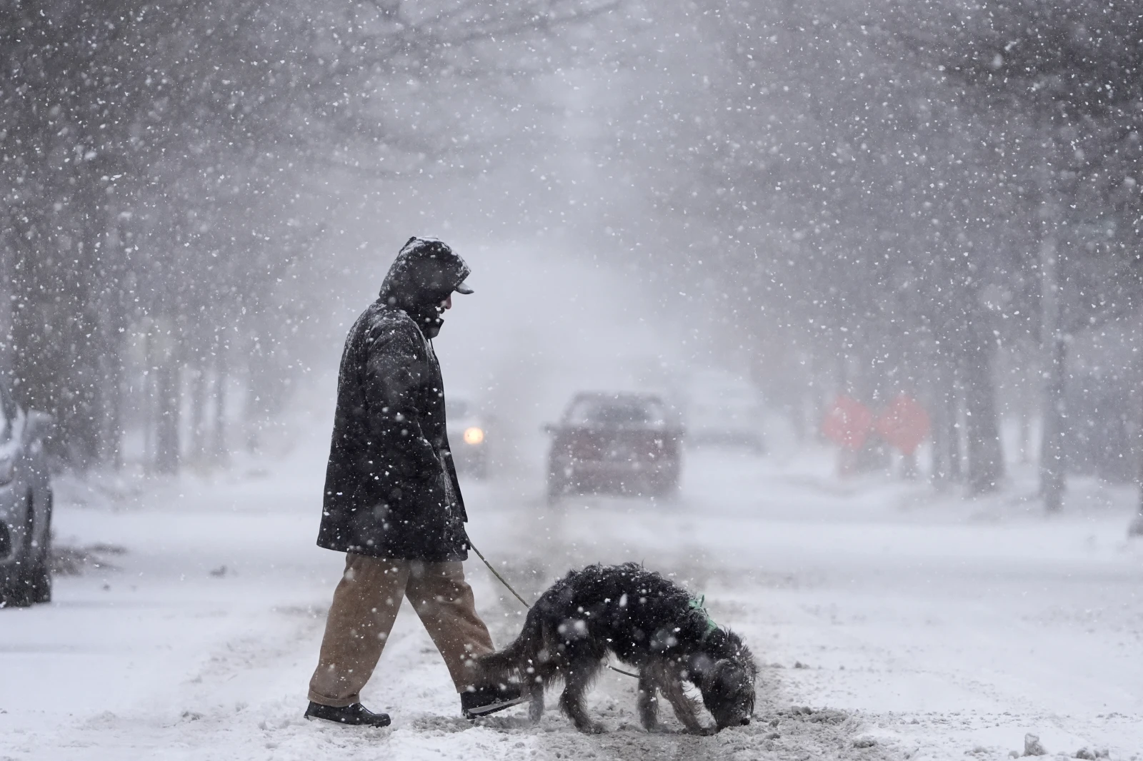 Enrique Davila crosses the street with his dog, Chula, as heavy snow falls Sunday, Jan. 5, 2025, in St. 